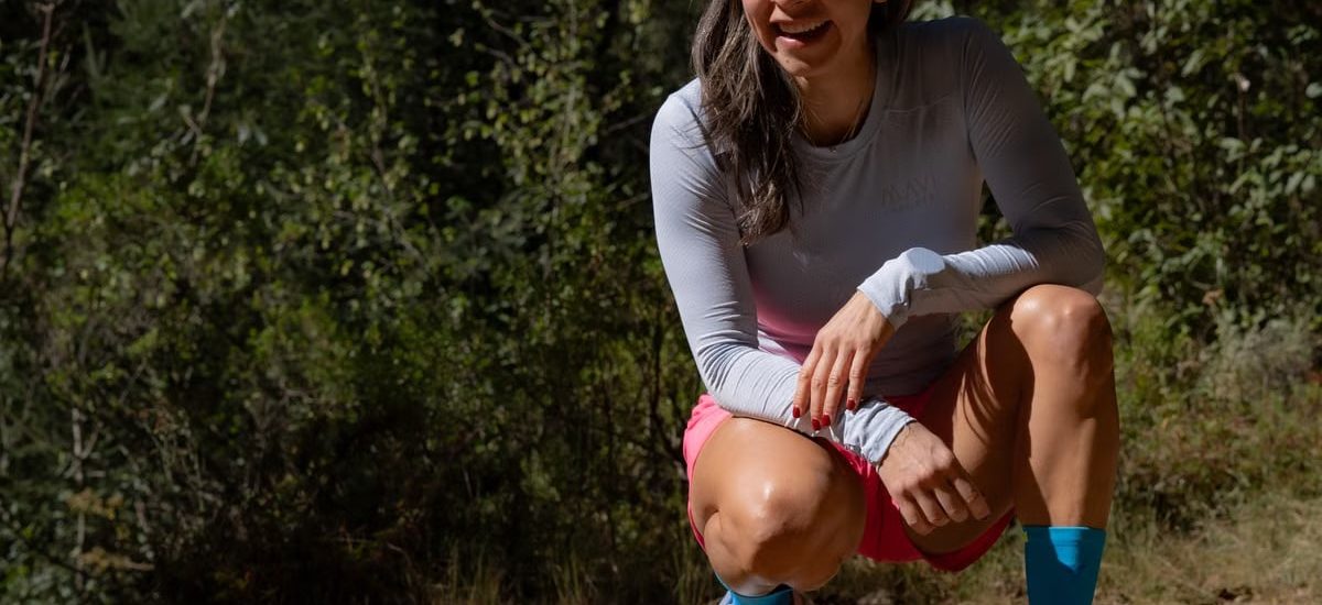 Smiling woman in sportswear takes a break during an outdoor workout, surrounded by nature.