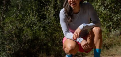 Smiling woman in sportswear takes a break during an outdoor workout, surrounded by nature.